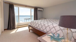 A bedroom with a large bed, a view of the sea, and a small table by the window. - The View at Lodi Point - Cozy Comfort On Level Lake Front! (Lodi)