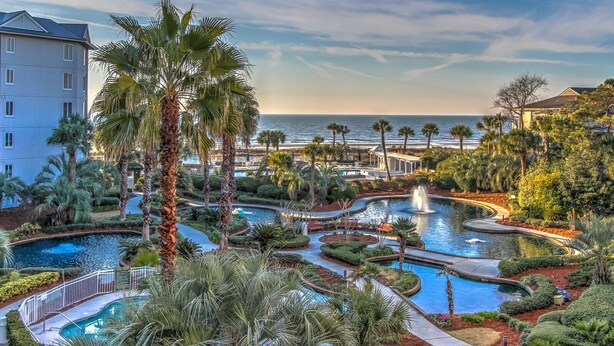 A resort with multiple swimming pools, palm trees, and a view of the ocean. - 1303 SeaCrest - 3rd Floor - Gorgeous Ocean Views & Walk to Shopping & Dining (Hilton Head Island)
