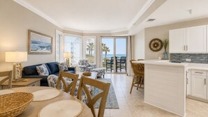 A modern living room with a sofa, chairs, a dining table, and a kitchen area with a view of the ocean. - 1303 SeaCrest - 3rd Floor - Gorgeous Ocean Views & Walk to Shopping & Dining (Hilton Head Island)