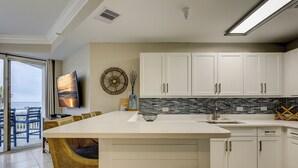 A modern kitchen with white cabinets, a large island, and a dining area with wicker chairs. - 1303 SeaCrest - 3rd Floor - Gorgeous Ocean Views & Walk to Shopping & Dining (Hilton Head Island)