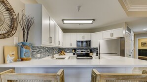 A modern kitchen with white cabinets, a central island, a built-in microwave, and a refrigerator. - 1303 SeaCrest - 3rd Floor - Gorgeous Ocean Views & Walk to Shopping & Dining (Hilton Head Island)