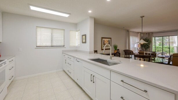 A modern kitchen with white cabinetry, a large island with a sink, and a dining area with a table and chairs.