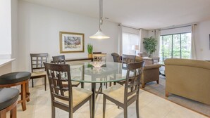 A dining area with a glass table surrounded by wooden chairs, a hanging light fixture, and a framed picture on the wall.