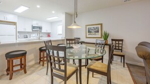 A modern kitchen with white cabinets, a microwave, and a glass dining table with chairs.