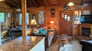 A cozy cabin interior with a wooden ceiling, a sofa, a coffee table, and a television. - On Beach Time – Vintage Cottage Near the Surf (Florence)