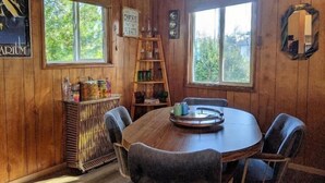 A wooden interior with a round table, chairs, a bar area, and large windows. - On Beach Time – Vintage Cottage Near the Surf (Florence)