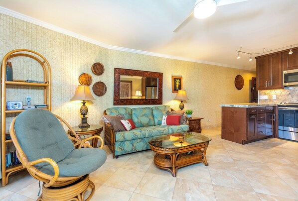 A living room with a sofa, armchair, and coffee table, a kitchen area with cabinets and appliances, and a dining table with chairs.