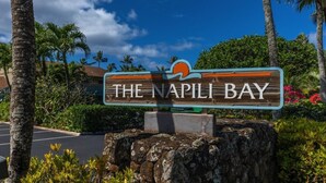 Un panneau en bois sur lequel est inscrit « The Napili Bay », entouré de verdure et de palmiers.