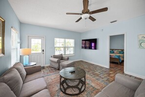 A living room with a ceiling fan, a sofa, a coffee table, a TV, and a patterned rug.