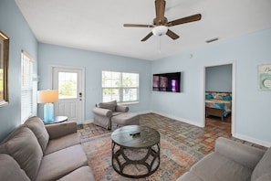 Un salon avec un ventilateur de plafond, un canapé, une table basse, un téléviseur et un tapis à motifs.