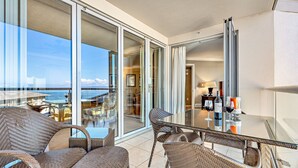 Un balcon agrémenté de meubles en osier, d’une table en verre et offrant une vue sur l’océan.