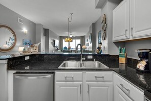 Uma cozinha moderna com bancada de granito preto, armários brancos e eletrodomésticos de aço inoxidável.