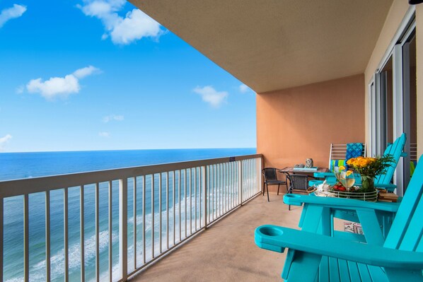 Een balkon met turquoise stoelen, een tafel met drankjes en uitzicht op de oceaan.