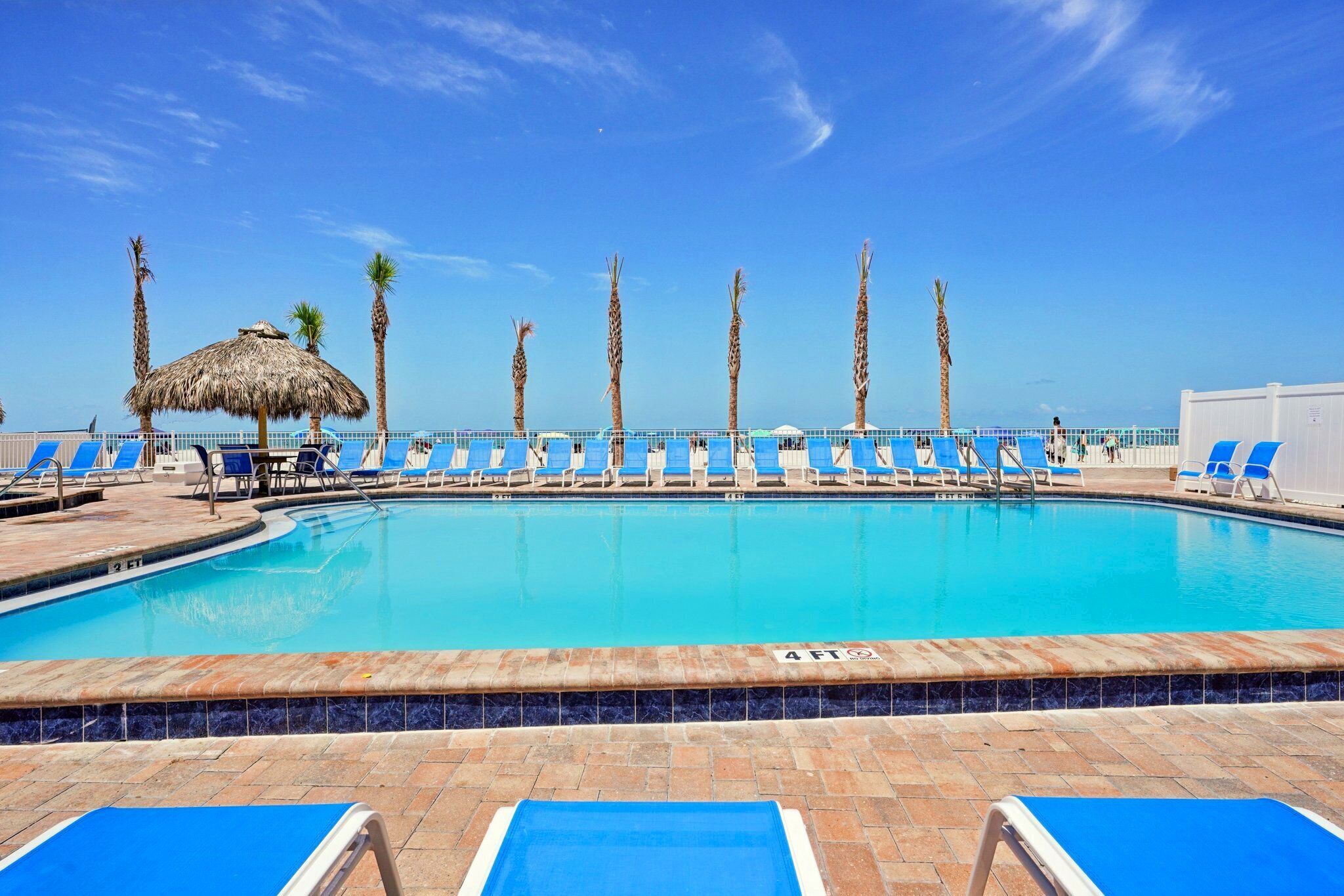 A swimming pool with blue lounge chairs and palm trees.