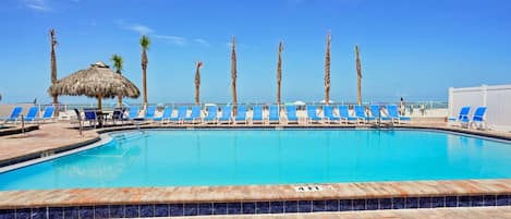A swimming pool with blue lounge chairs and palm trees.
