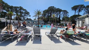 A poolside area with lounge chairs and a swimming pool, surrounded by trees and a building. - Bay View,  Villa Golf Cart, Private Deck, Blue Bayou 270 Fairways (Miramar Beach)