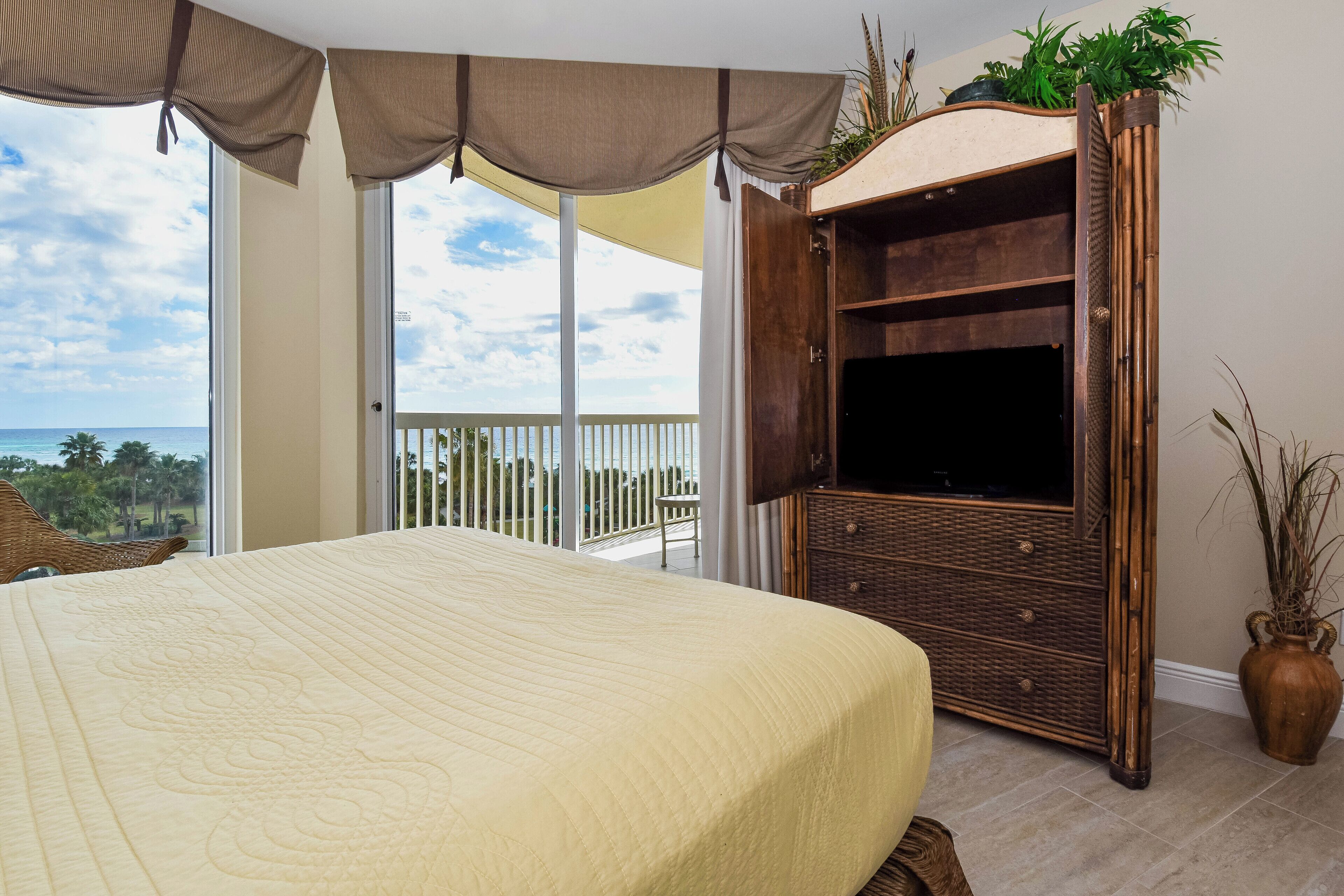 Un dormitorio con una cama grande, un armario de madera con un televisor y un balcón con vistas al océano.
