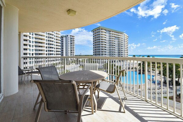 A balcony with a table and chairs, overlooking a pool and high-rise buildings.