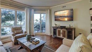 Ein Wohnzimmer mit großem Fernseher, einem Glastisch und Blick ins Freie.