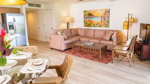 Un salon moderne avec un canapé d’angle, une table à manger avec des chaises, une table basse en verre et un tableau accroché au mur.