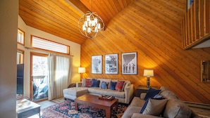 Un salon chaleureux avec un plafond en bois, un canapé d’angle, une table basse et un tapis à motifs.