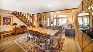 Un grand espace de vie comprenant un escalier en bois, une table à manger avec des chaises, un canapé et un coin cuisine.