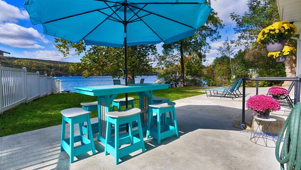 Un espace extérieur aménagé avec des meubles de couleur turquoise, comprenant une table et des chaises, un grand parasol et des plantes en pot.