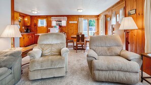 Un intérieur de chalet chaleureux avec deux fauteuils, une table à manger et un coin cuisine.