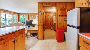 L’intérieur d’une cabane avec des murs en bois, un coin cuisine équipé d’un réfrigérateur, une table à manger et un téléviseur.