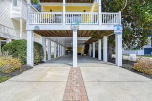 Un passage couvert mène à un bâtiment doté d’un balcon, une pancarte indique la présence d’une piscine privée, et un numéro de téléphone est fourni pour toute demande de renseignements concernant la location.