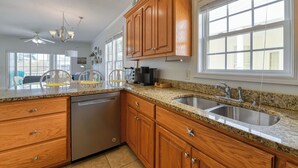 A kitchen with wooden cabinets, granite countertops, a dishwasher, and a double sink. - A Wave from it All - Five Bedroom, Four Bath Beach House (Surfside Beach)