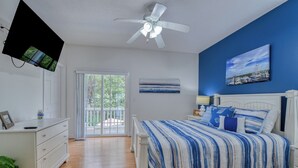 A bedroom with a bed, a ceiling fan, a TV mounted on the wall, and a view of the outdoors through a sliding door. - A Wave from it All - Five Bedroom, Four Bath Beach House (Surfside Beach)