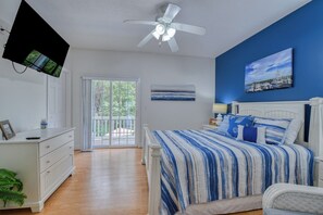 Quarto com cama, ventoinha no teto, televisão fixada na parede e vista para o exterior por uma porta de correr.