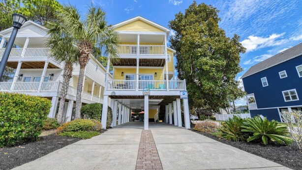 A multi-story hotel with a covered entrance, balconies, and a clear sky. - A Wave from it All - Five Bedroom, Four Bath Beach House (Surfside Beach)