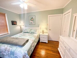 Een slaapkamer met een bed, nachtkastjes, een dressoir en een plafondventilator.