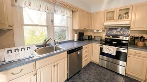 A kitchen with light wooden cabinets, a stainless steel dishwasher, a double oven, and a window with a decorative curtain. - Piece of Paradise-Pet Friendly-Walk to restaurants&shopping. (Cape May)