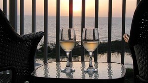 Una mesa con dos copas de vino en un balcón con vista al mar al atardecer.