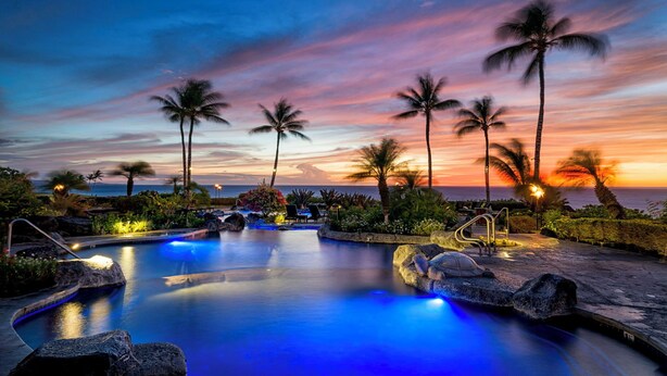 A pool area with a sunset view, palm trees, and a stone pathway. - 🏖️Oceanfront Hali'i Kai Penthouse | 3BR Sunset Views (Waikoloa)