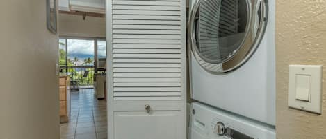 A laundry room with a washing machine and dryer, a door leading to a balcony with outdoor furniture, and a tiled floor.