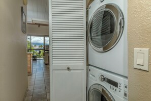 Un lavadero con lavadora y secadora, una puerta que da a un balcón con mobiliario exterior, y suelo de baldosas.