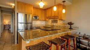 Una cocina con armarios de madera, electrodomésticos de acero inoxidable, encimera de granito y taburetes de bar.