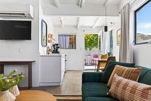 Un saló modern amb un sofà verd, una televisió de pantalla plana i una zona de cuina amb una màquina de cafè.