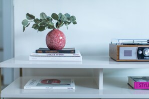 Une étagère blanche avec des livres, un vase rouge avec des feuilles vertes et une radio en bois.