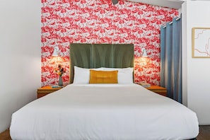 A hotel room with a bed, two bedside tables, a green upholstered headboard, and a wall with a red and white flamingo pattern. - Communal Pool + Hot Tub | Dining + Spas + Joshua Tree | The Rosalie (Palm Springs)