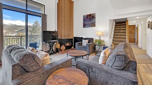 A spacious living room with a fireplace, comfortable seating, and a large window offering a mountain view.