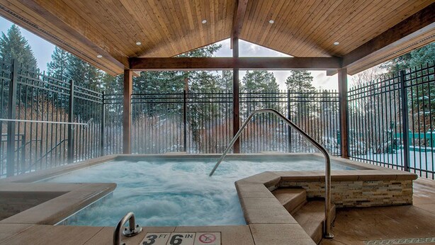 A hot tub area with a wooden ceiling, metal railings, and a view of trees outside.