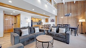 A spacious living area with two grey sofas, a round coffee table, and a wooden dining table with chairs.