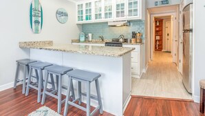 Una cocina con una isla central, taburetes de bar, armarios blancos, un reloj y una decoración con una tabla de surf.