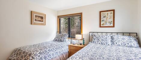 A bedroom with two beds, a window, and framed pictures on the walls.