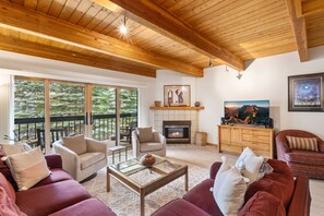 Un salón con chimenea, techo de madera y ventanas grandes.